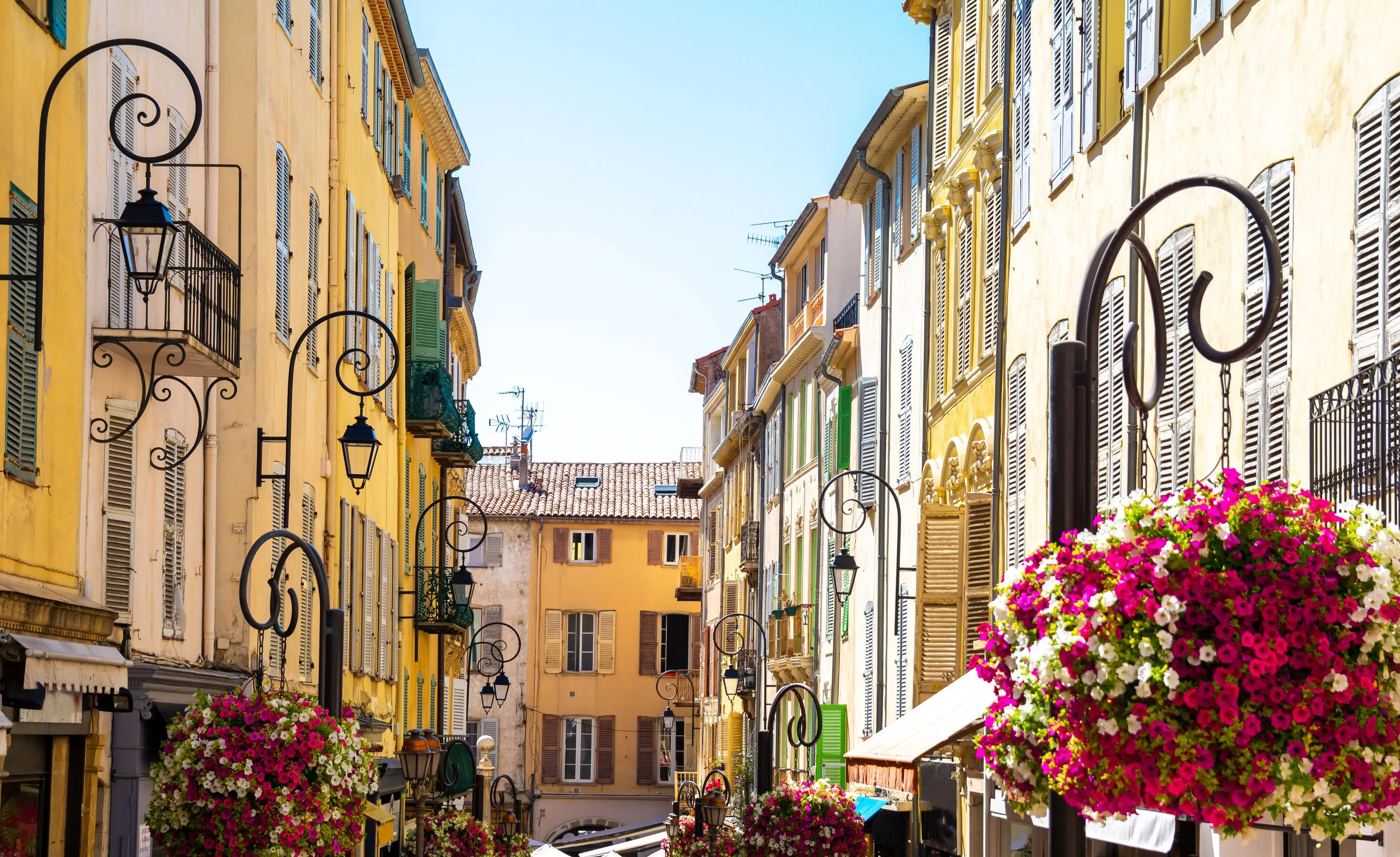 Une ruelle fleurie de la vieille ville d’Antibes, façades ocre et lanternes en fer forgé