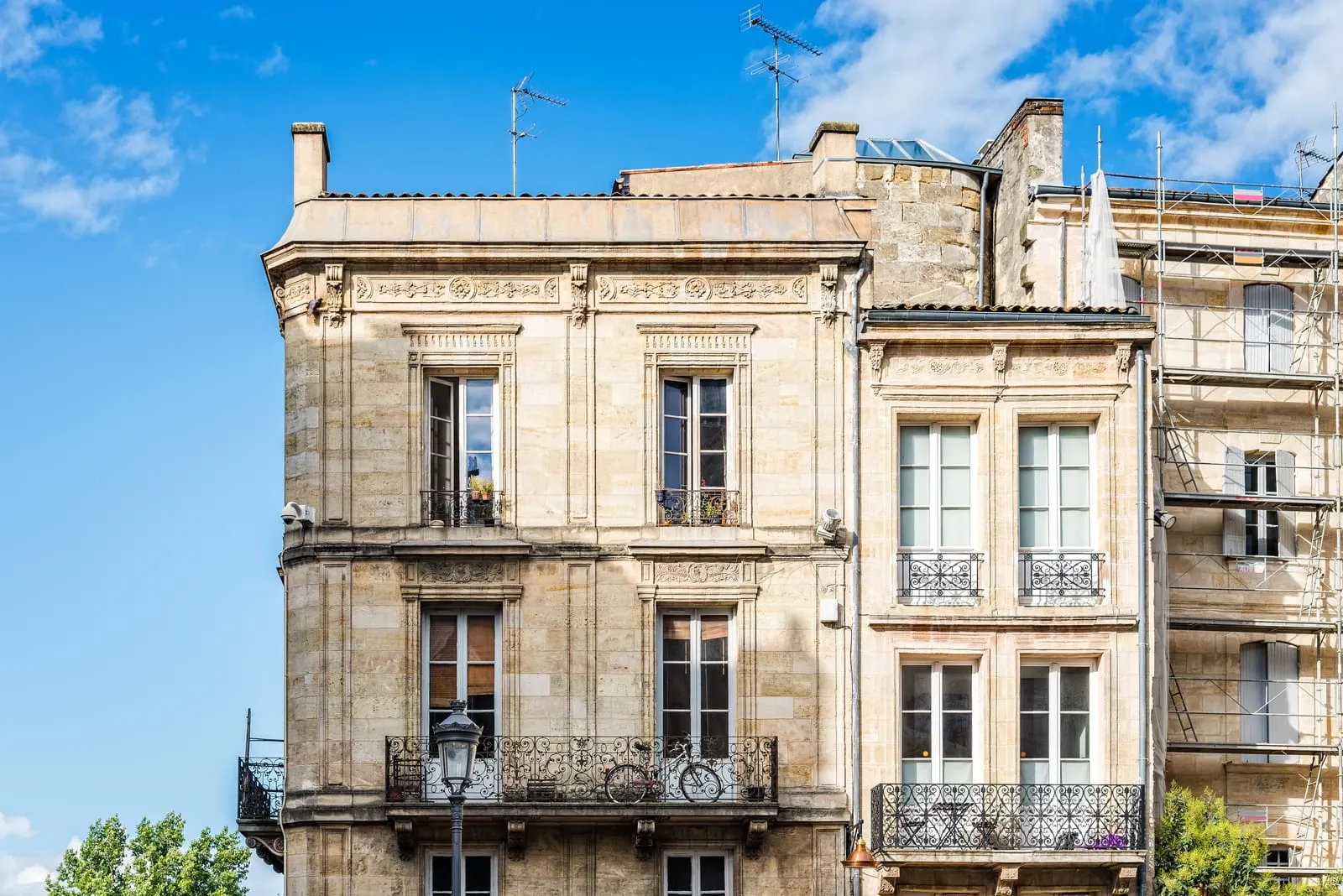 Deux immeubles en pierre blonde du XVIIIe et leurs balcons en fer forgé, sous un ciel bleu, à Bordeaux