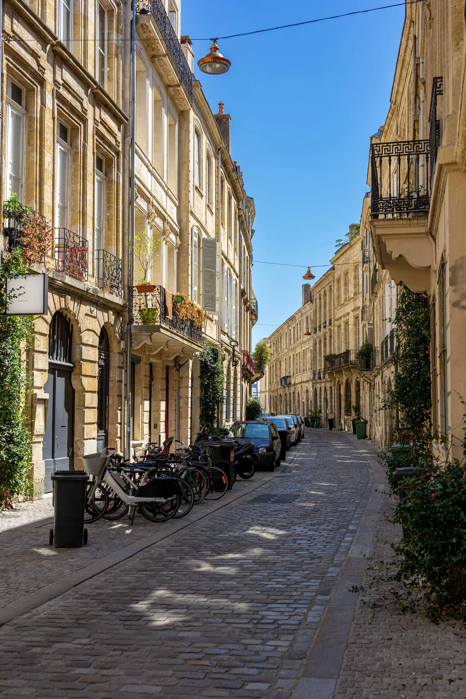 Une rue étroite du vieux Bordeaux, façades en pierre, balcons, vélos et voitures garés