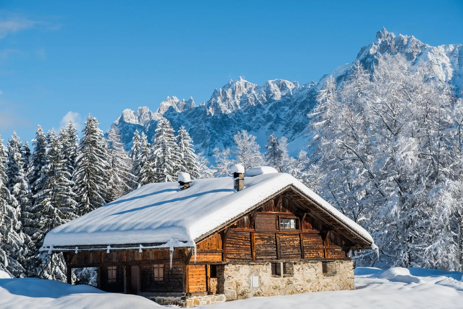 Un chalet de bois sous la neige face aux aiguilles de Chamonix