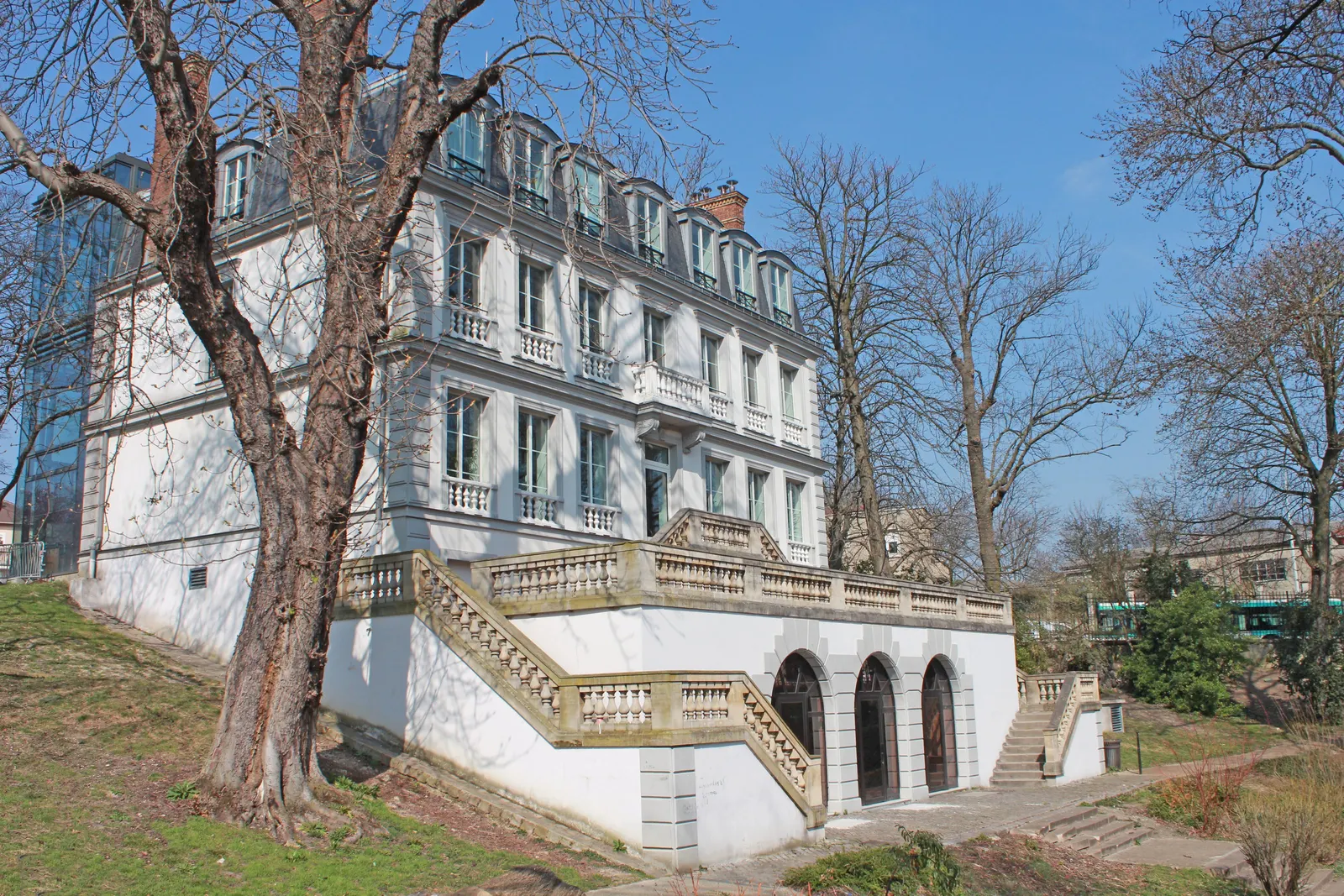 The château de l’Étang in Bagnolet, its white façade and its stone staircase among tall trees
