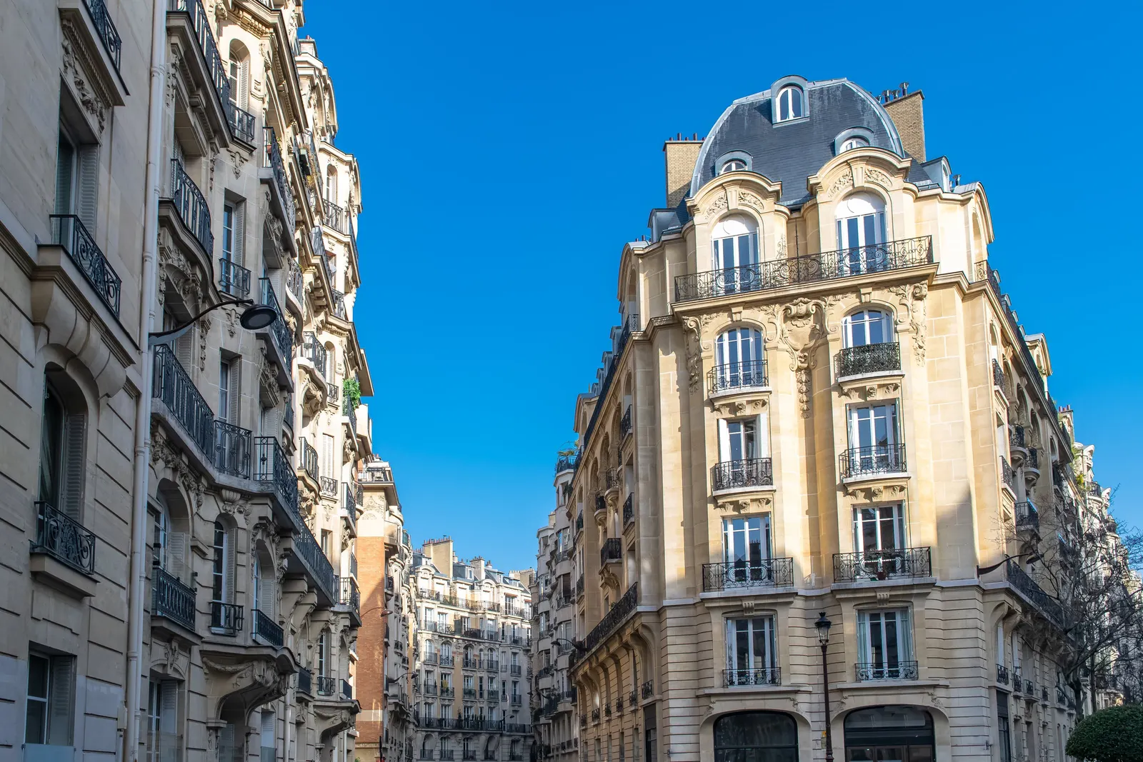 Stone apartment buildings in Neuilly-sur-Seine, their wrought-iron balconies and slate roofs under a deep blue sky