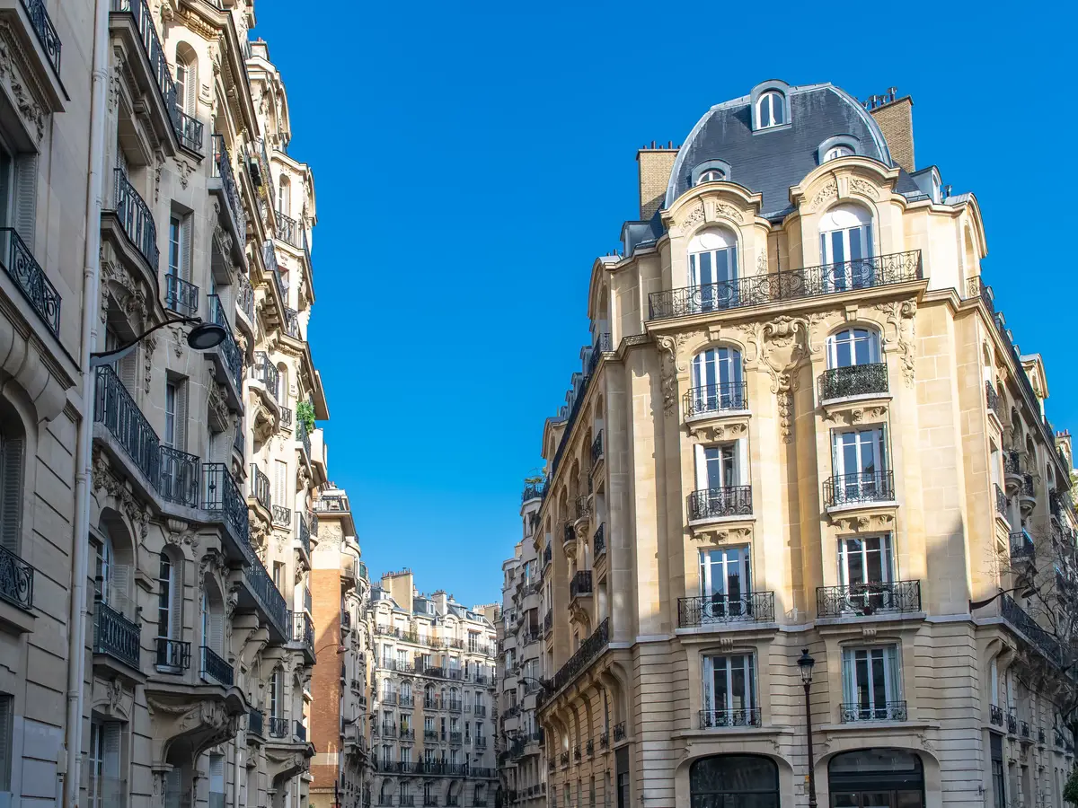 Stone apartment buildings in Neuilly-sur-Seine, their wrought-iron balconies and slate roofs under a deep blue sky