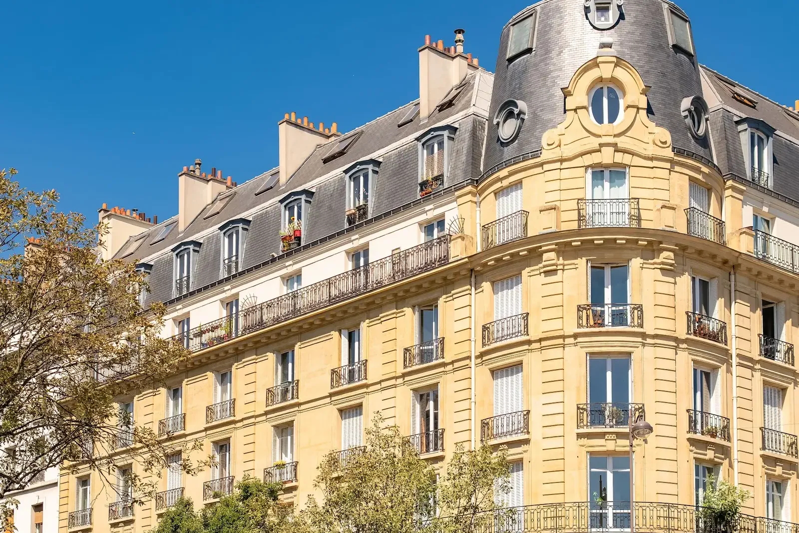 Angle d’un immeuble haussmannien en pierre de taille baigné de soleil, à Paris
