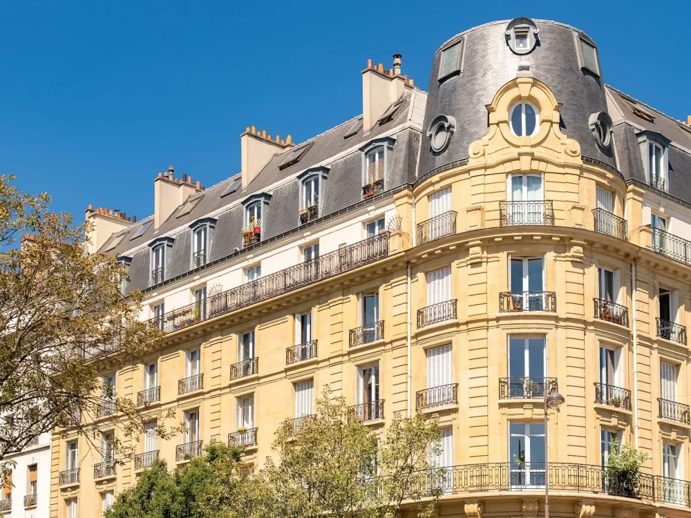 Angle d’un immeuble haussmannien en pierre de taille baigné de soleil, à Paris
