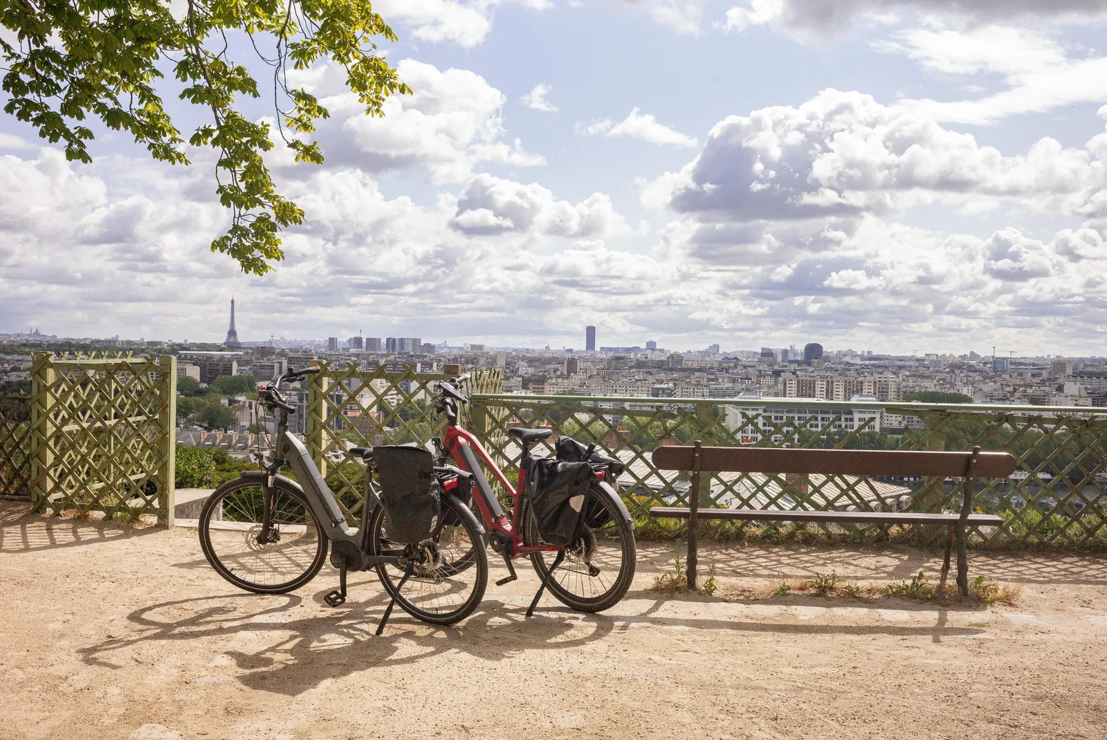 Two bicycles and a bench on the terrace of the Saint-Cloud park, facing the rooftops of Paris and the Eiffel Tower under a cloudy sky