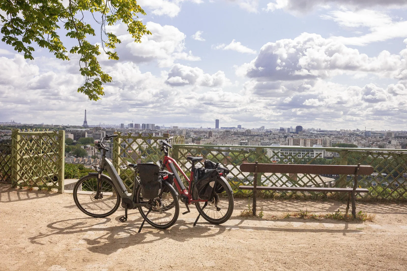Duas bicicletas e um banco no terraço do parque de Saint-Cloud, de frente para os telhados de Paris e a torre Eiffel sob um céu de nuvens