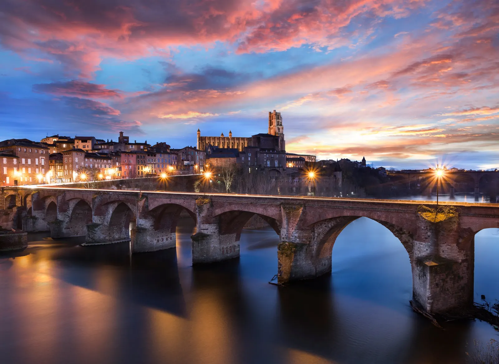 The Pont-Vieux over the Tarn and Albi’s Sainte-Cécile cathedral at sunset, under a pink and blue sky