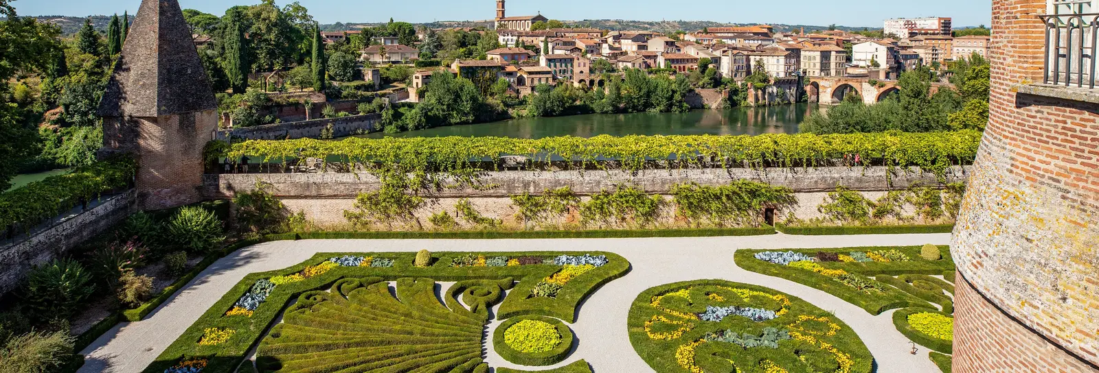 Albi vu des jardins du palais de la Berbie, leurs parterres fleuris au-dessus du Tarn, le vieux pont et les maisons de brique de l’autre rive