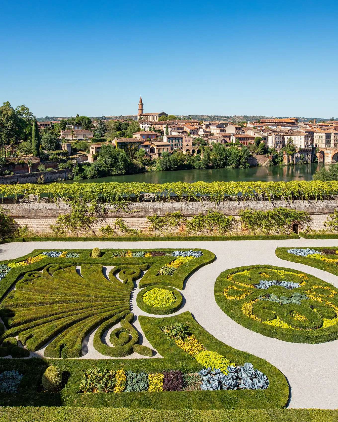 Albi vu des jardins du palais de la Berbie, leurs parterres fleuris au-dessus du Tarn, le vieux pont et les maisons de brique de l’autre rive