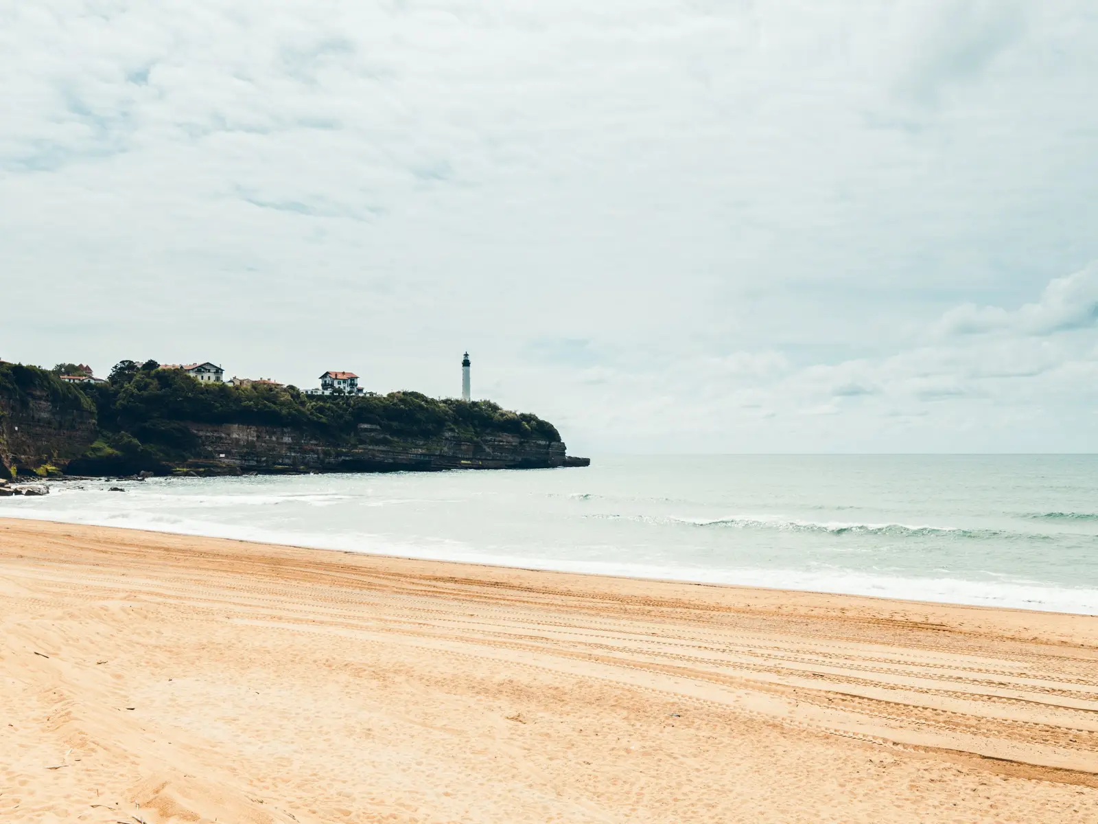 Uma grande praia de Anglet virada para o oceano, a falésia e o farol de Biarritz ao longe