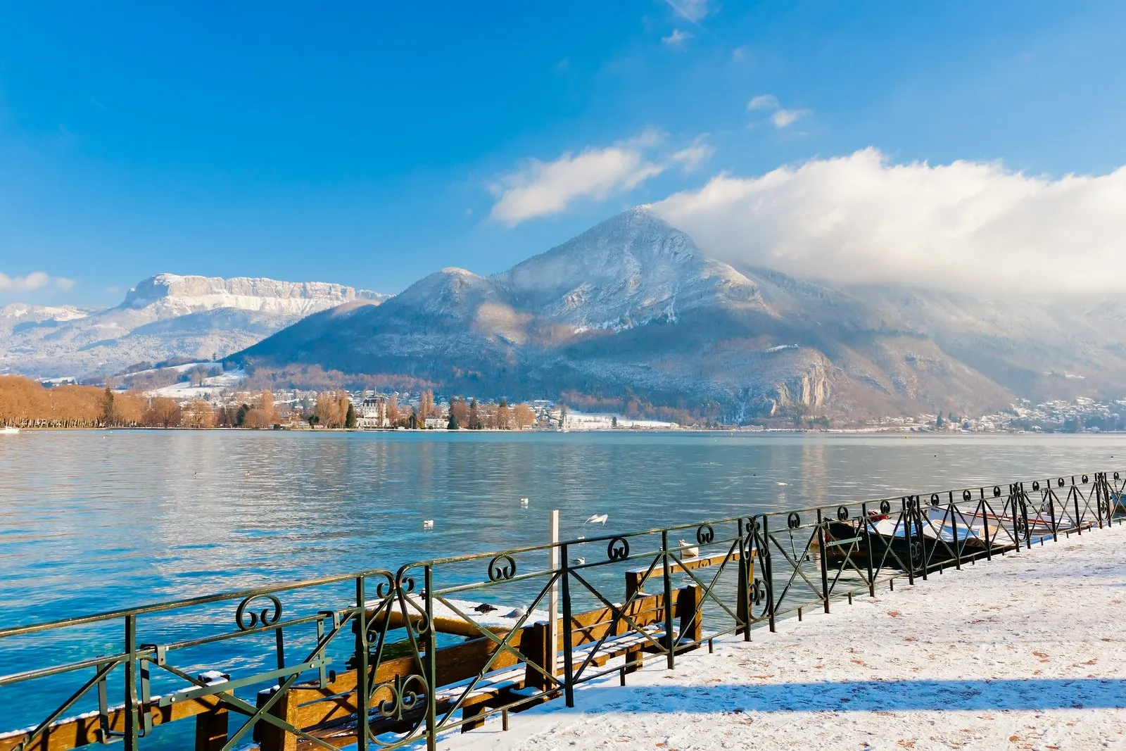 O cais nevado do lago de Annecy e os cumes no inverno