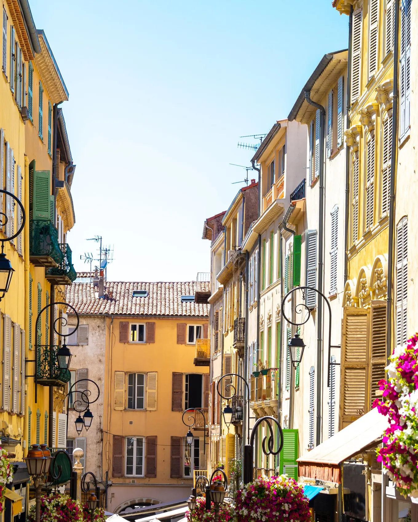 Uma ruela florida da cidade velha de Antibes, fachadas ocre e lanternas de ferro forjado