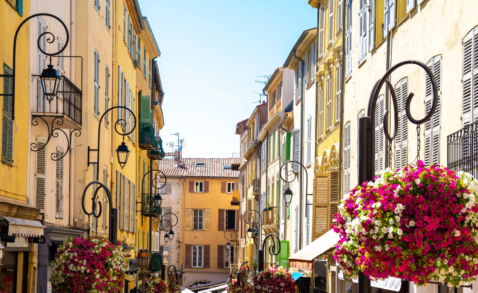 Une ruelle fleurie de la vieille ville d’Antibes, façades ocre et lanternes en fer forgé