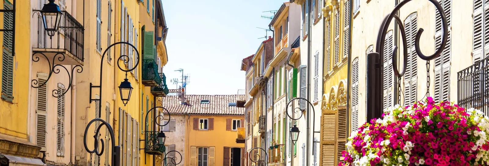 Uma ruela florida da cidade velha de Antibes, fachadas ocre e lanternas de ferro forjado
