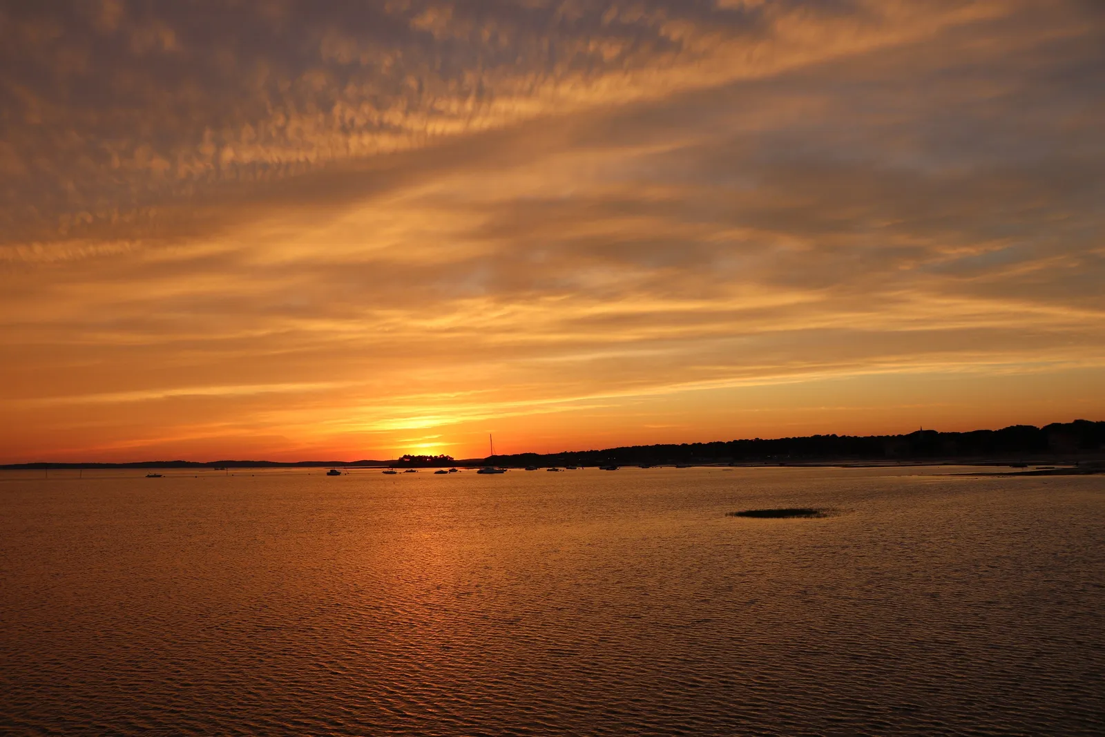 Le bassin d’Arcachon au coucher du soleil, le ciel orangé au-dessus de la rive opposée