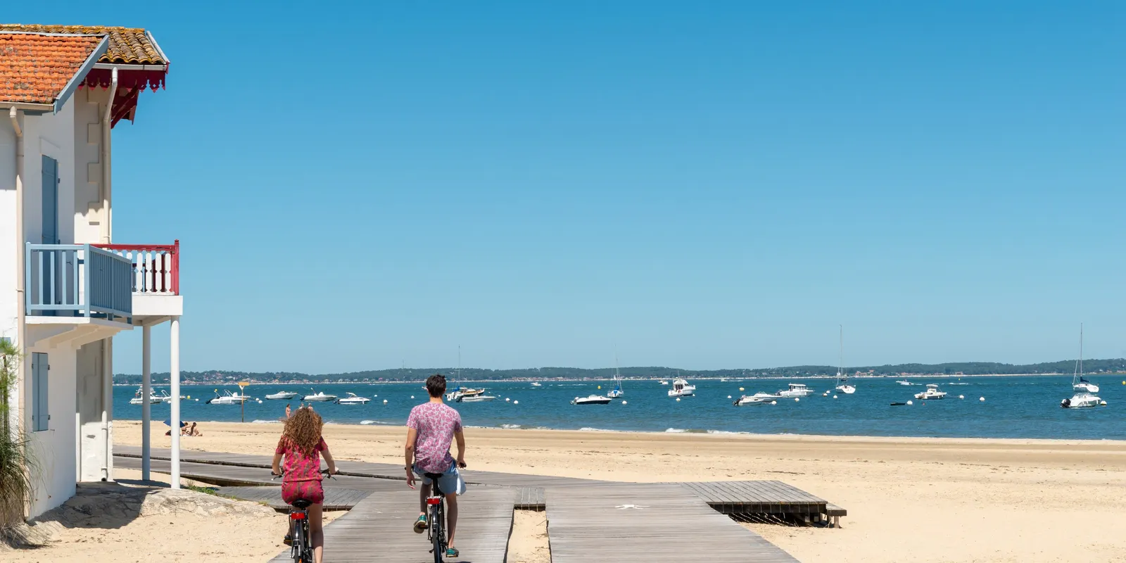 Une villa du front de mer d’Arcachon, la promenade de bois sur la plage et deux cyclistes face au bassin