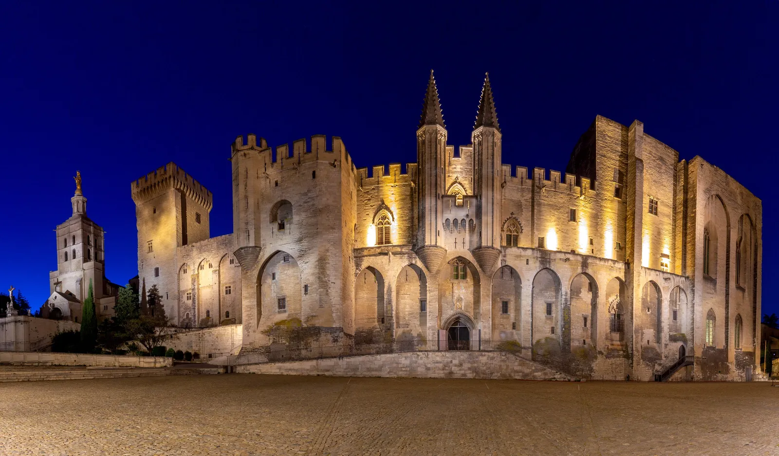 O palácio dos Papas de Avignon iluminado à noite, e o campanário da catedral de Notre-Dame-des-Doms