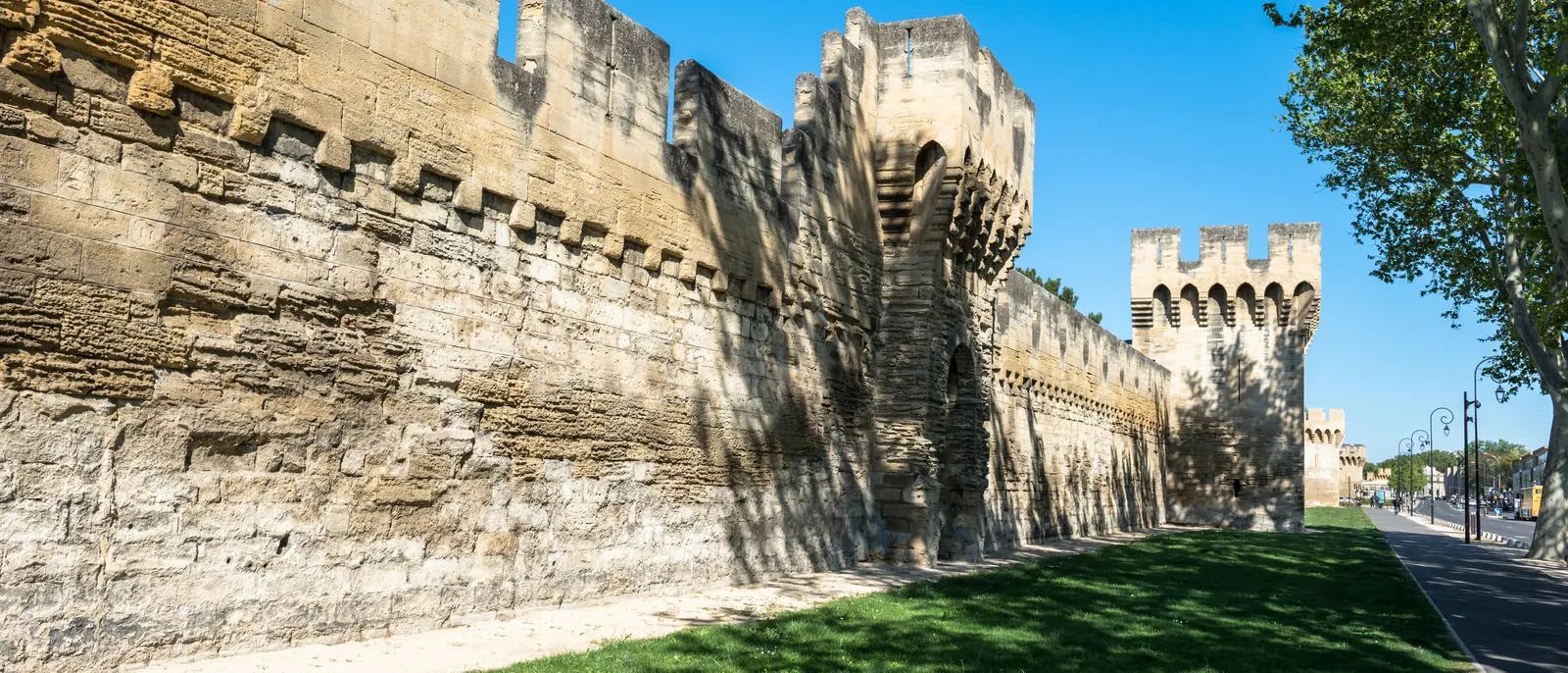 Les remparts d’Avignon, leurs créneaux et leurs tours de pierre au-dessus d’une pelouse, sous le ciel bleu