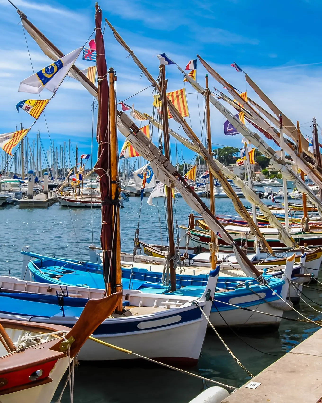 Traditional pointu boats dressed with flags at the quay in the port of Bandol, their masts and pennants under a blue sky