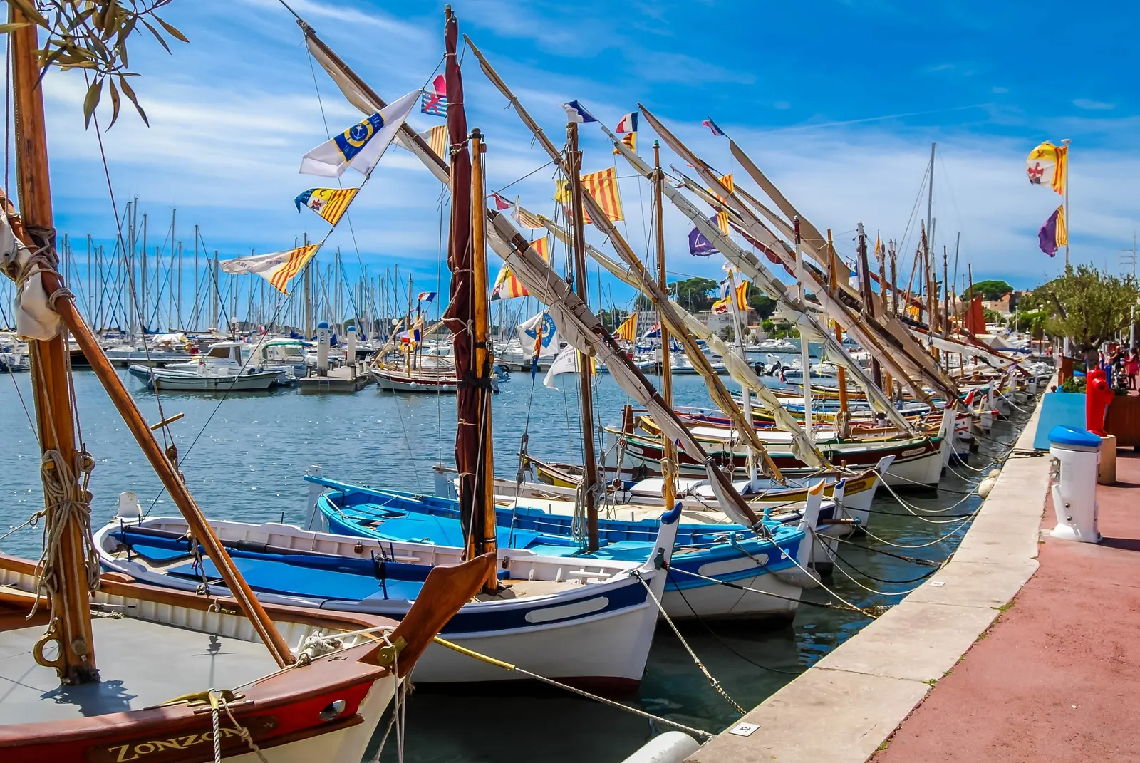 Traditional pointu boats dressed with flags at the quay in the port of Bandol, their masts and pennants under a blue sky