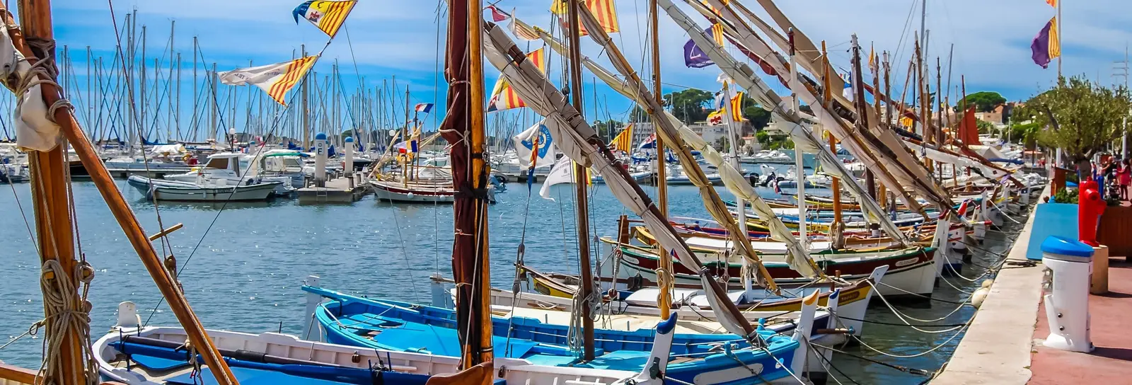 Traditional pointu boats dressed with flags at the quay in the port of Bandol, their masts and pennants under a blue sky