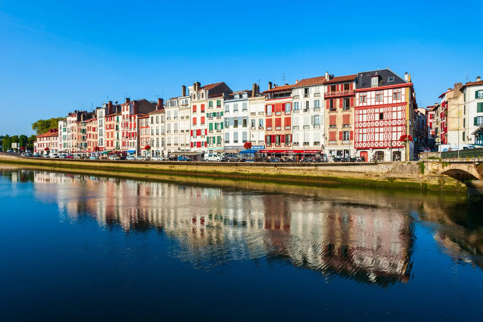 As altas fachadas de enxaimel e persianas vermelhas dos cais do Nive em Bayonne, refletidas no rio