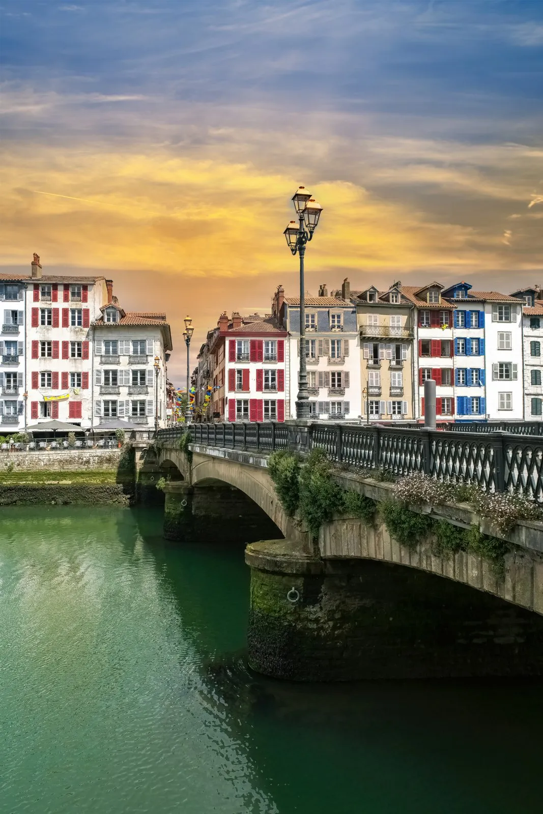 Uma ponte sobre o Nive em Bayonne ao pôr do sol, os seus candeeiros e as fachadas coloridas dos cais