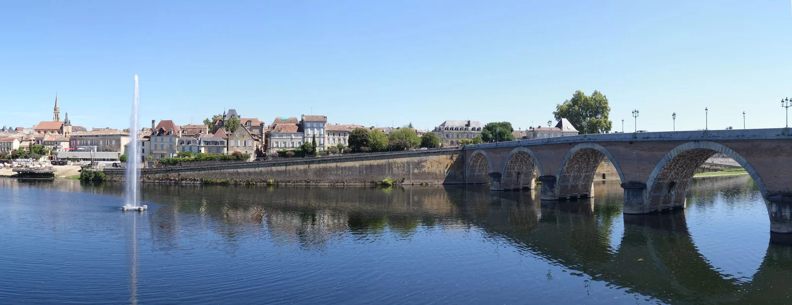 A cidade velha de Bergerac na margem do rio Dordonha, com os cais dominados por um campanário pontiagudo, um repuxo no meio do rio e a velha ponte de pedra de grandes arcos