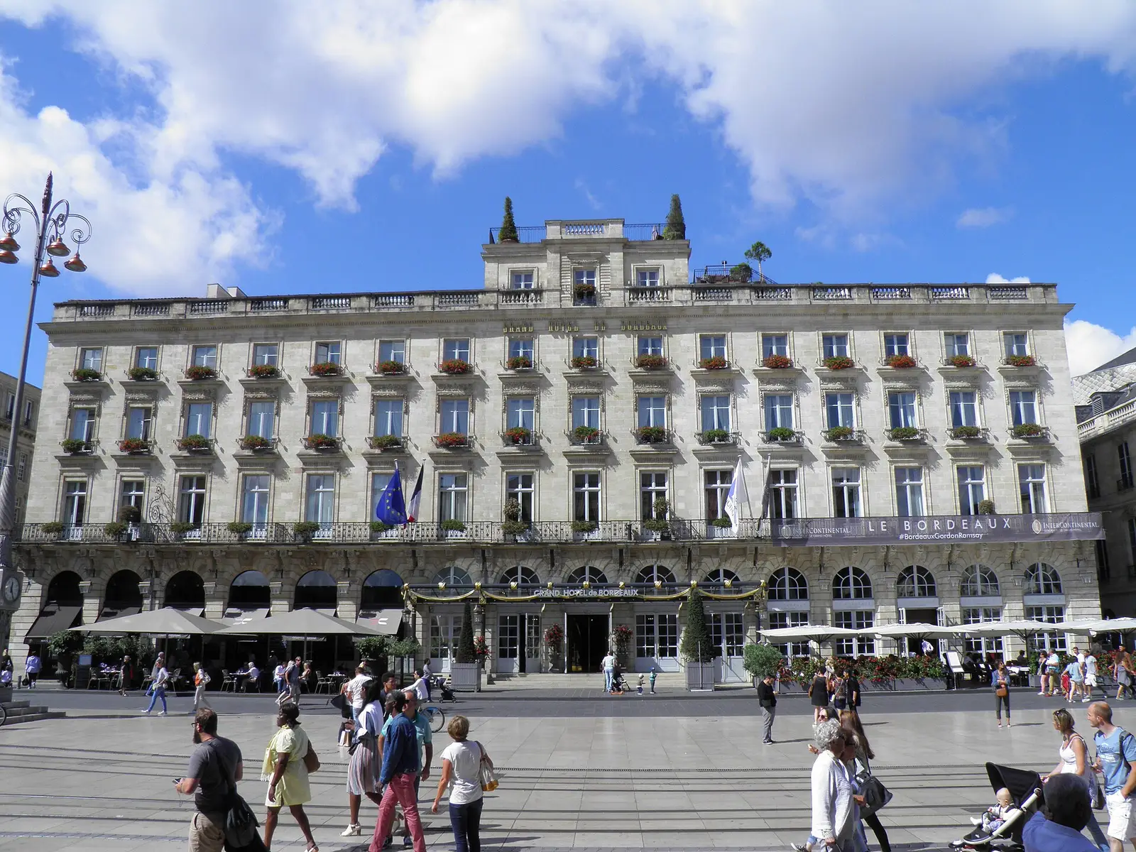 Edifício haussmanniano de Bordéus em pedra clara, arcadas e varandas floridas sobre uma praça animada