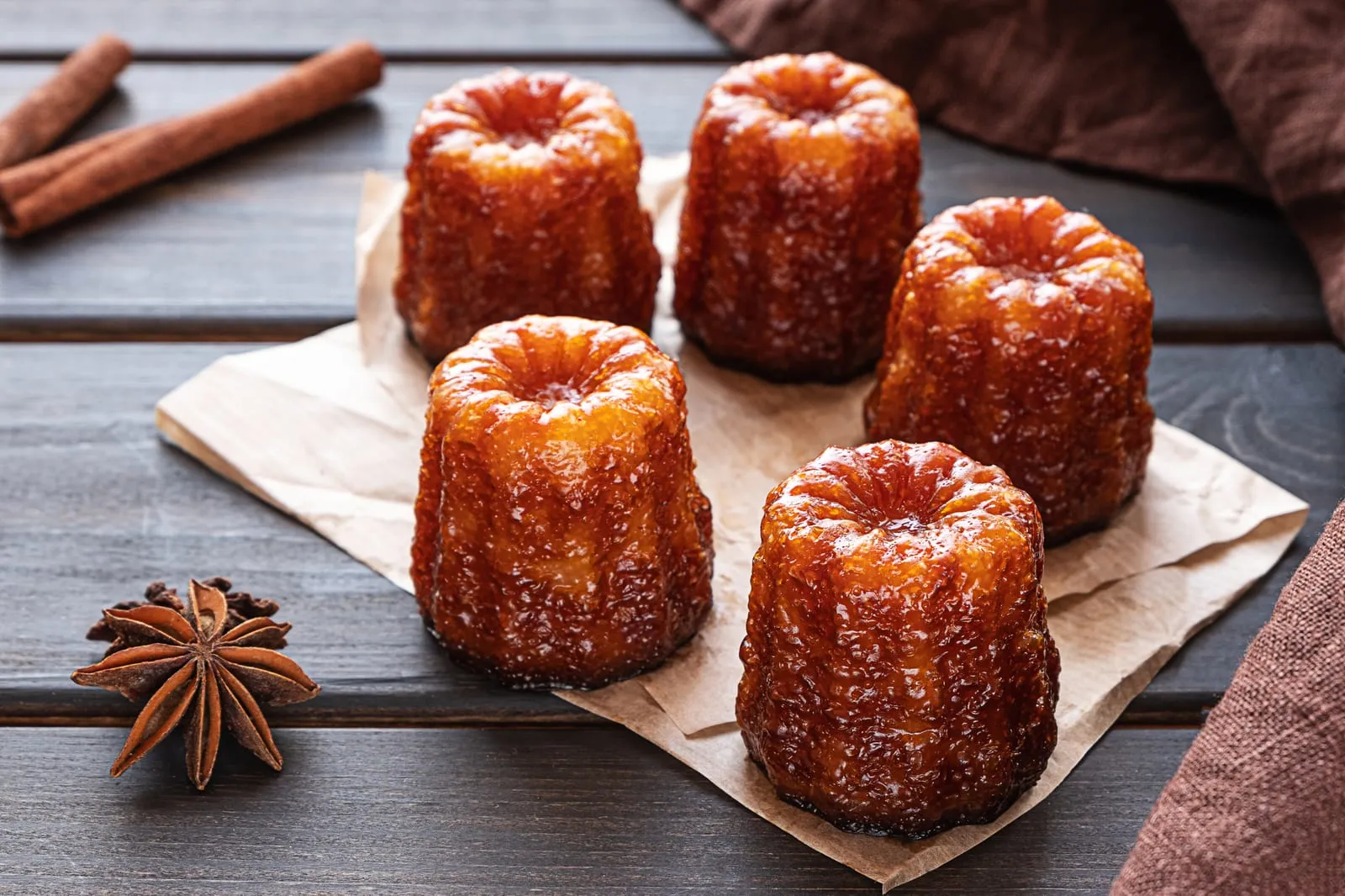 Des canelés bordelais posés sur du papier, avec cannelle et badiane