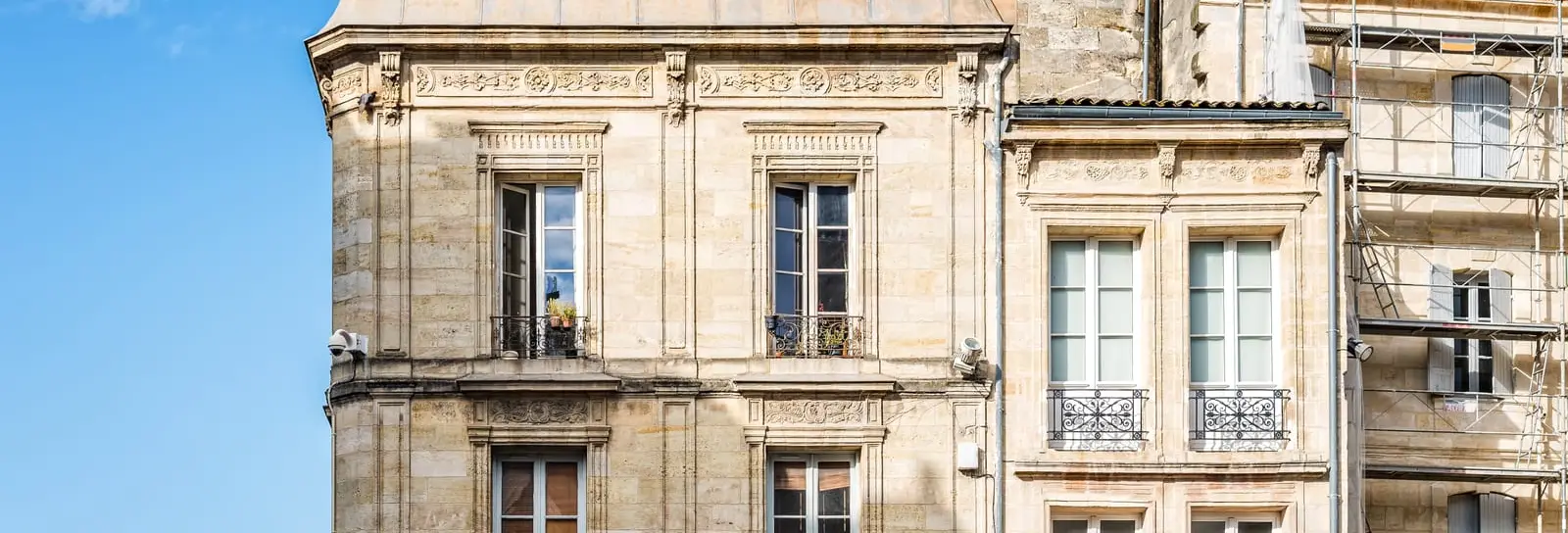 Deux immeubles en pierre blonde du XVIIIe et leurs balcons en fer forgé, sous un ciel bleu, à Bordeaux