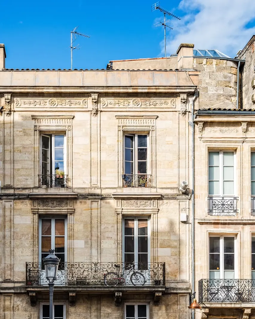 Two 18th-century buildings in honey-coloured stone and their wrought-iron balconies, under a blue sky, in Bordeaux