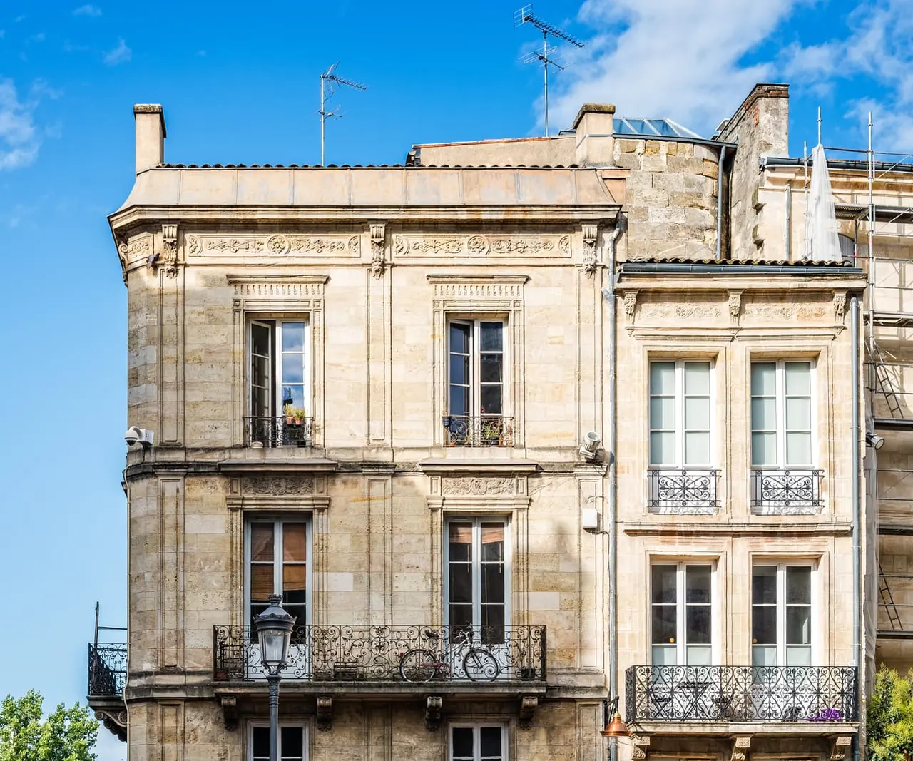 Deux immeubles en pierre blonde du XVIIIe et leurs balcons en fer forgé, sous un ciel bleu, à Bordeaux