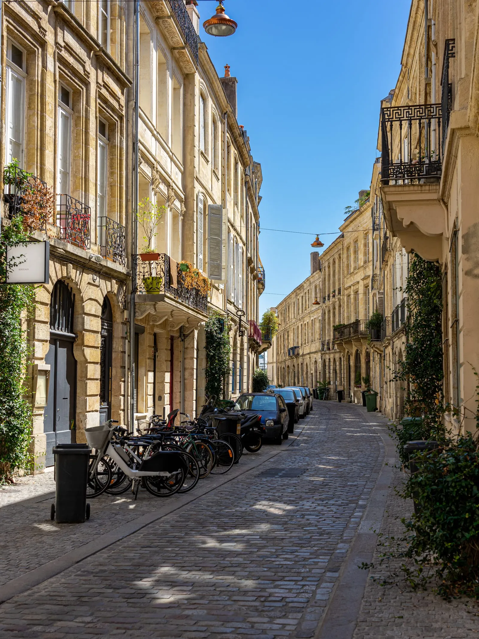 Une rue étroite du vieux Bordeaux, façades en pierre, balcons, vélos et voitures garés