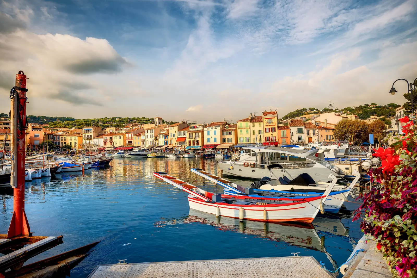 O porto de Cassis, os seus barcos de pesca e de recreio diante das fachadas coloridas do cais, buganvília em primeiro plano