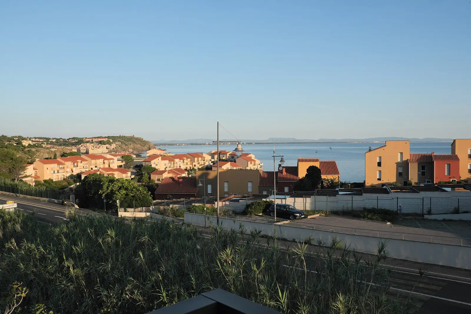 Toits de tuiles et façades ocres de Collioure, vus d’en haut vers la mer et les collines