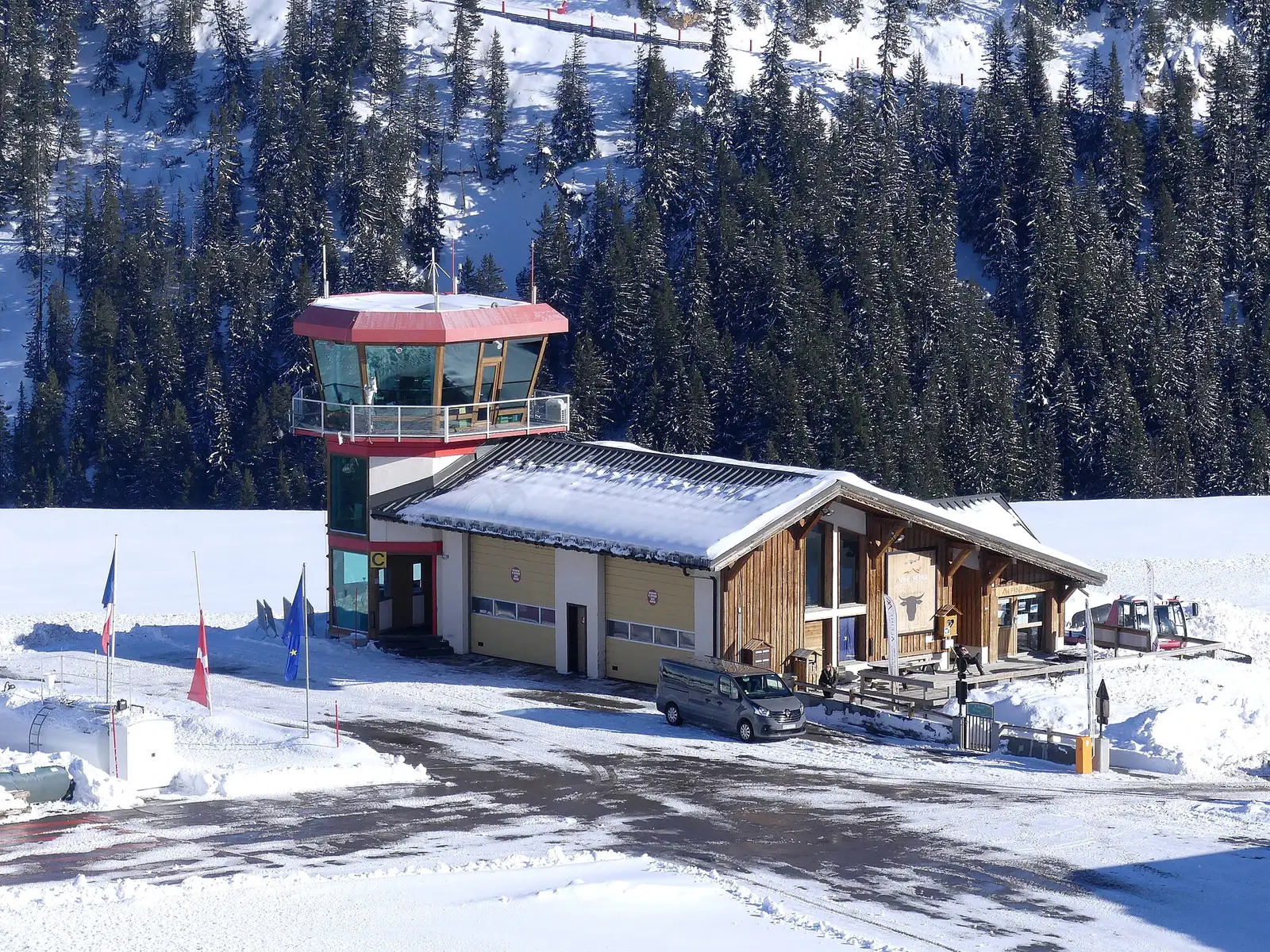 Station de Courchevel sous la neige, tour à toit rouge, chalet de bois et télésiège au-dessus des sapins