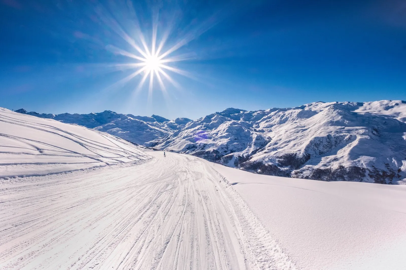 Une piste damée sous le soleil, les montagnes à l’horizon