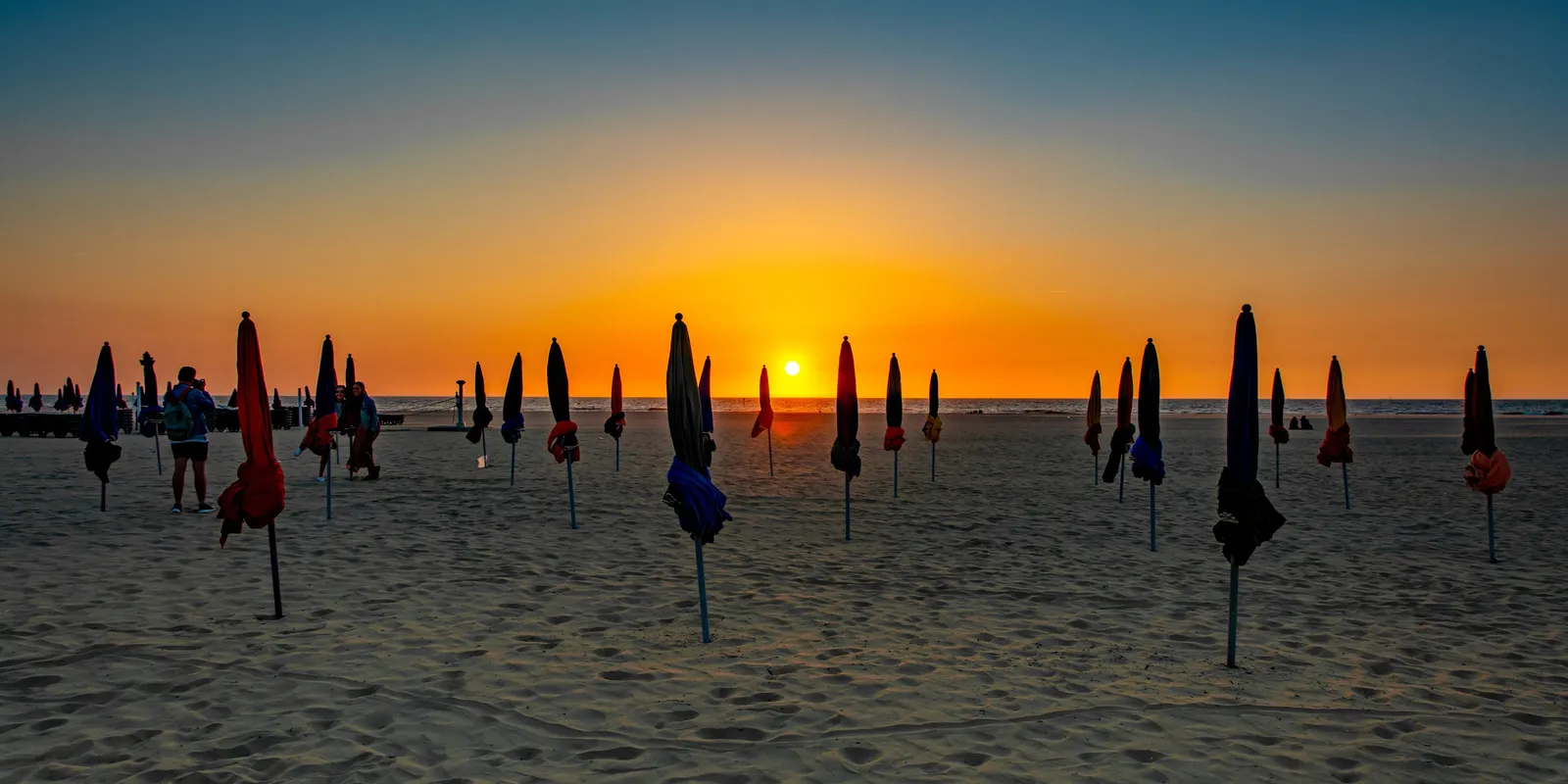 Os guarda-sóis fechados na praia de Deauville ao pôr do sol, ao longo da marginal
