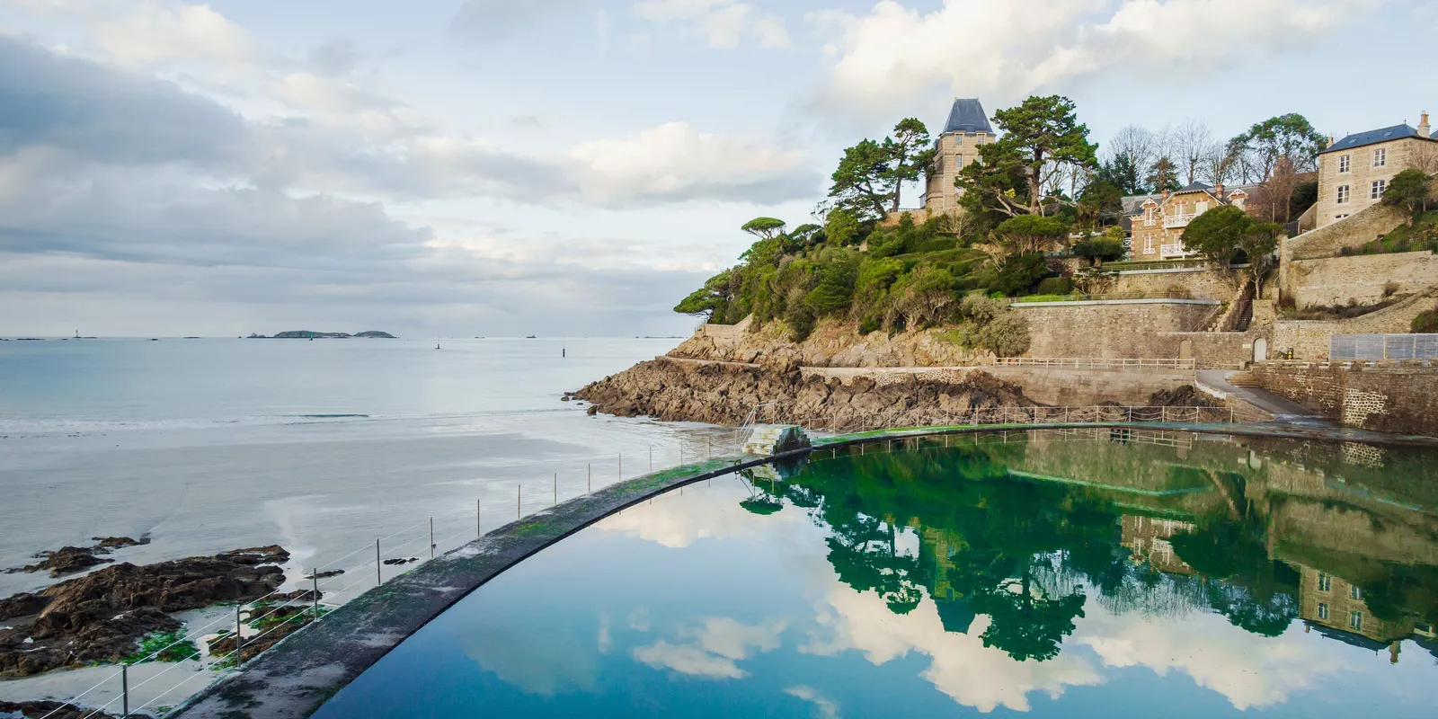 A piscina de água do mar da praia de l'Écluse e as villas da Pointe du Moulinet