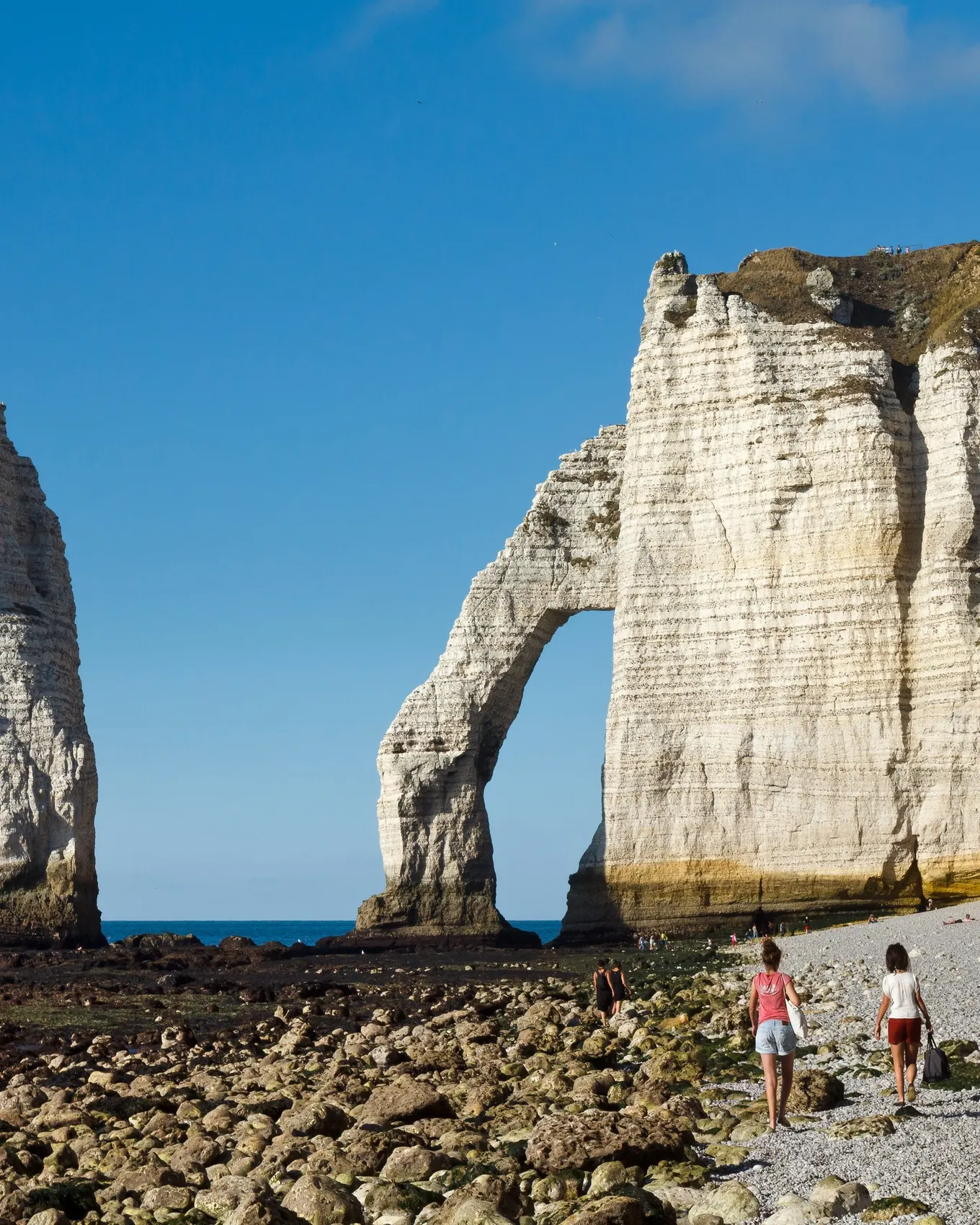 The Aiguille and the Porte d’Aval arch in Étretat seen from the shingle beach, under a blue sky