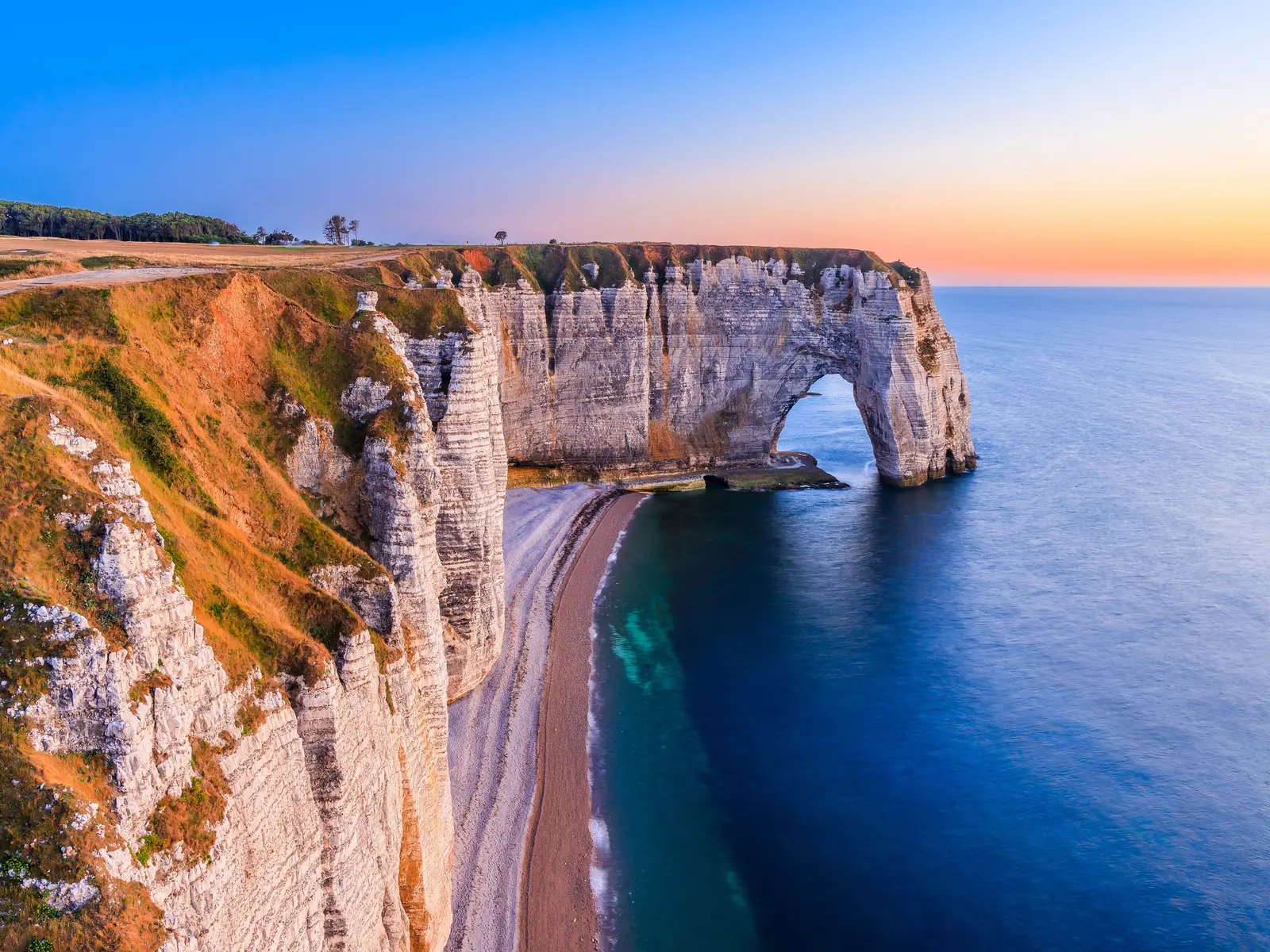 La Manneporte et la plage de la Valaine à Étretat au soleil couchant, la falaise de craie au-dessus de la mer bleue