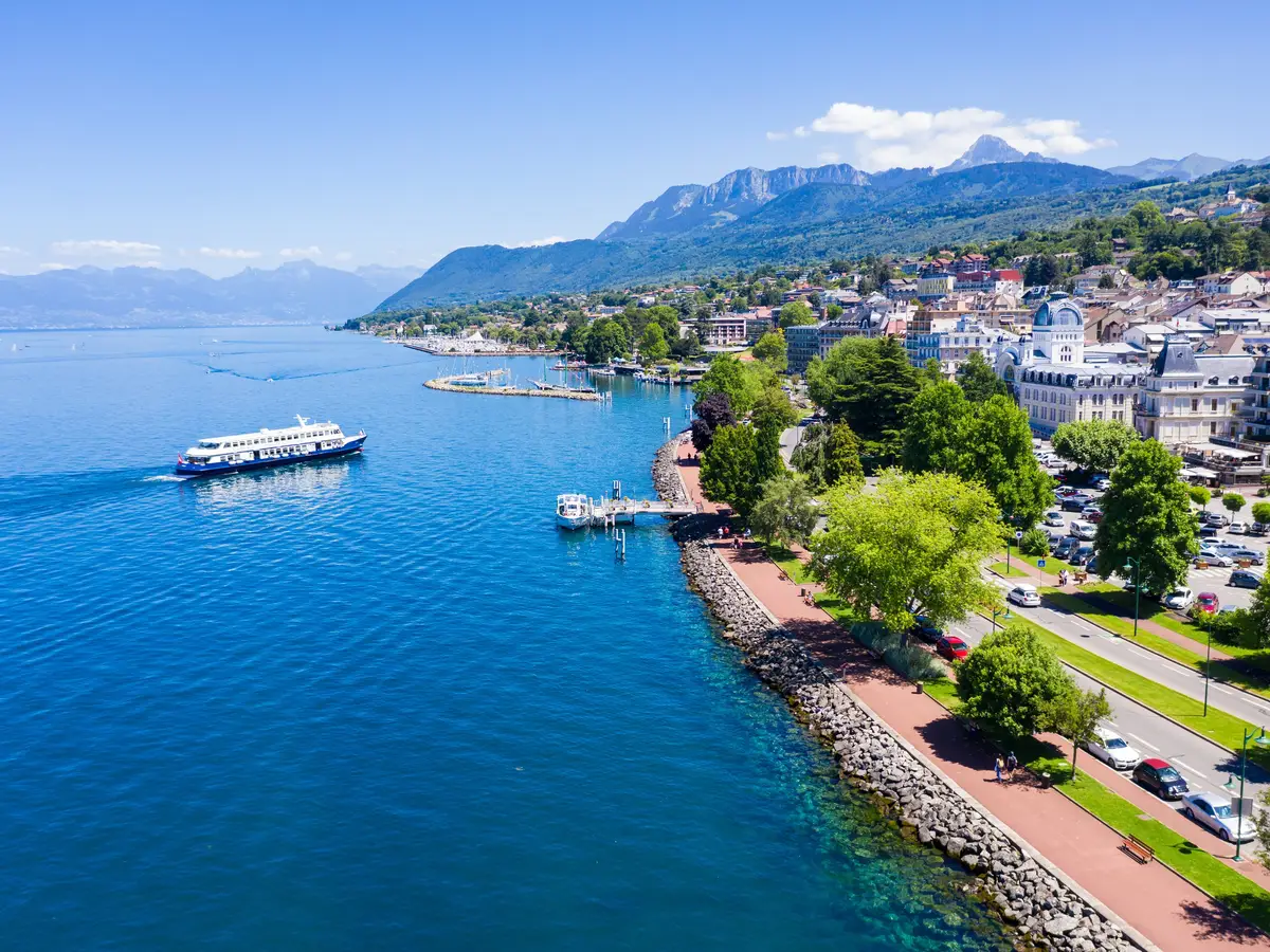 Les quais d’Évian-les-Bains vus du ciel : la promenade arborée au bord du Léman, le port et un bateau sur le lac