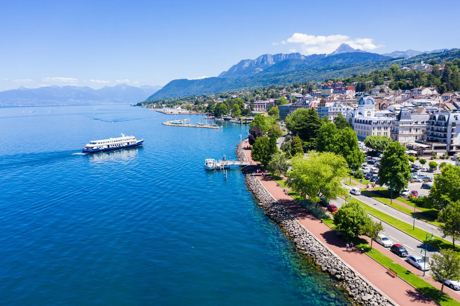The quays of Évian-les-Bains from the sky: the tree-lined promenade along Lake Geneva, the harbour and a boat on the lake