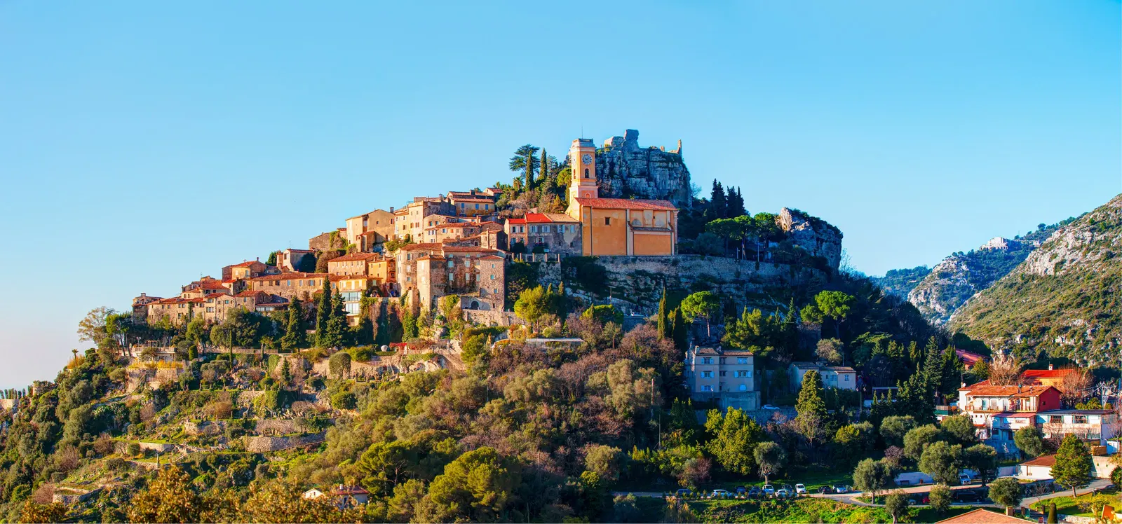 A aldeia empoleirada de Èze no seu pico rochoso, a igreja e as casas de pedra acima das encostas arborizadas