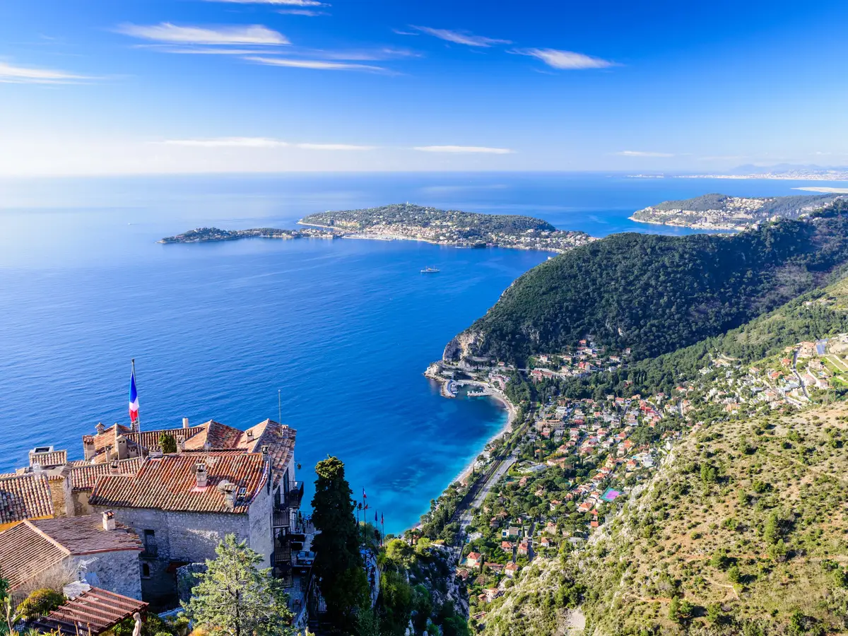 Èze village vu des hauteurs : ses toits de pierre au-dessus de la Méditerranée et la côte et ses caps à l’horizon