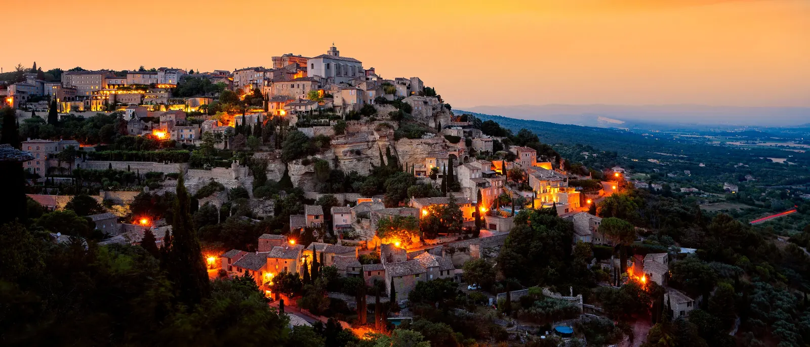 Gordes ao cair da noite, as ruelas iluminadas e dois balões no céu alaranjado