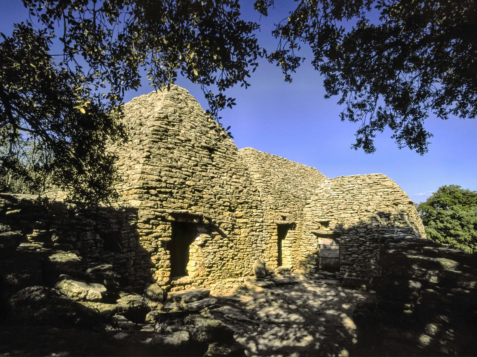 Le village des Bories à Gordes, ses cabanes de pierre sèche à l’ombre d’un chêne sous le ciel bleu