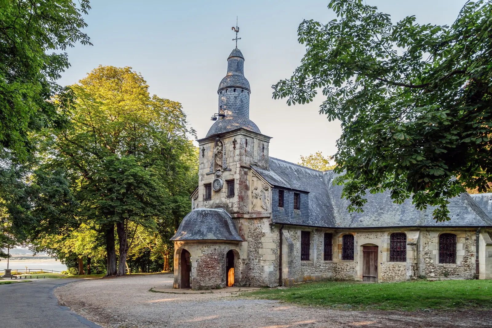 A capela Notre-Dame-de-Grâce em Honfleur, as suas paredes de pedra e o campanário revestido de ardósia, sob as árvores da Côte de Grâce